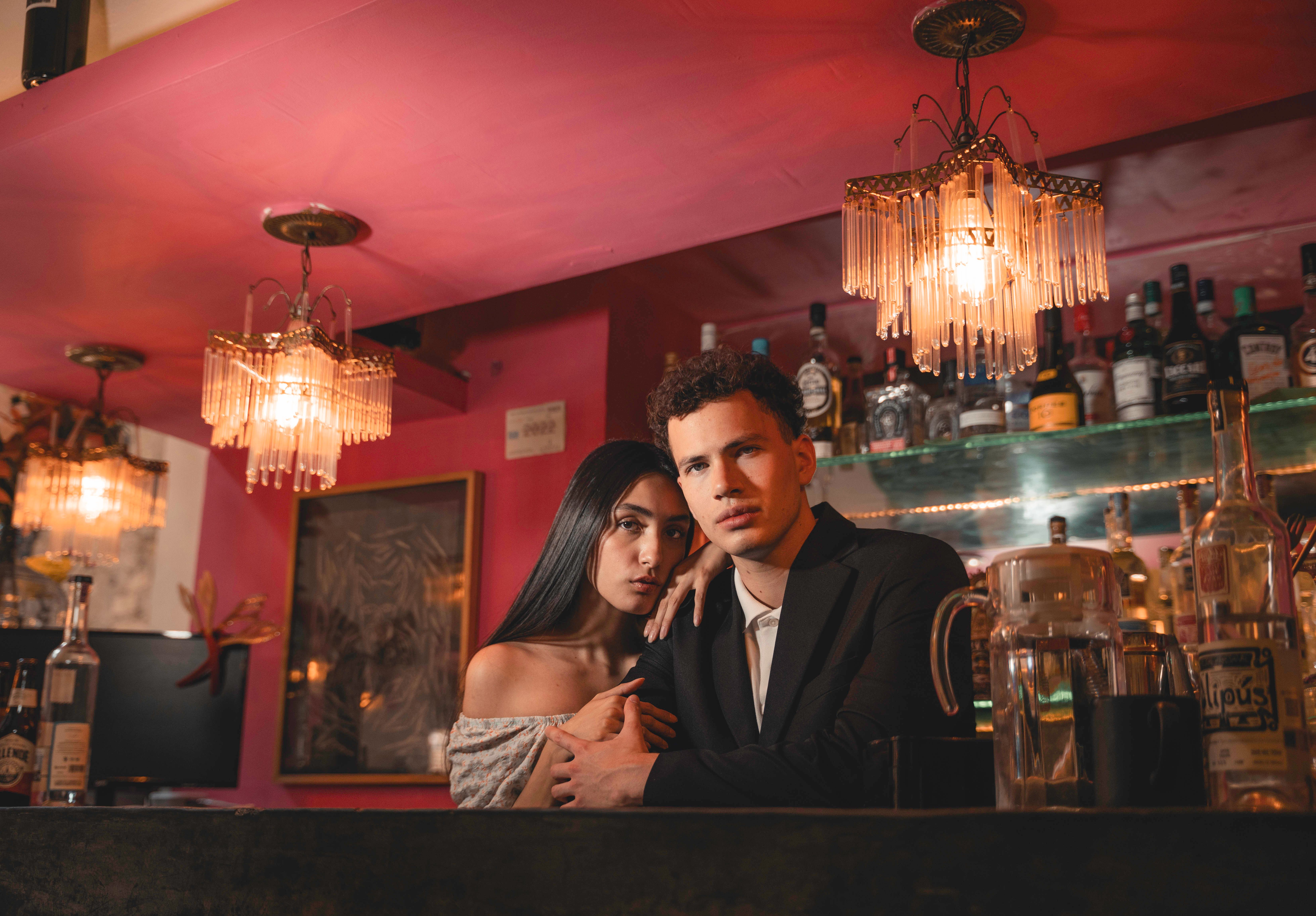 Stylish couple posing at a sophisticated cocktail bar illuminated by warm ambient chandelier lighting