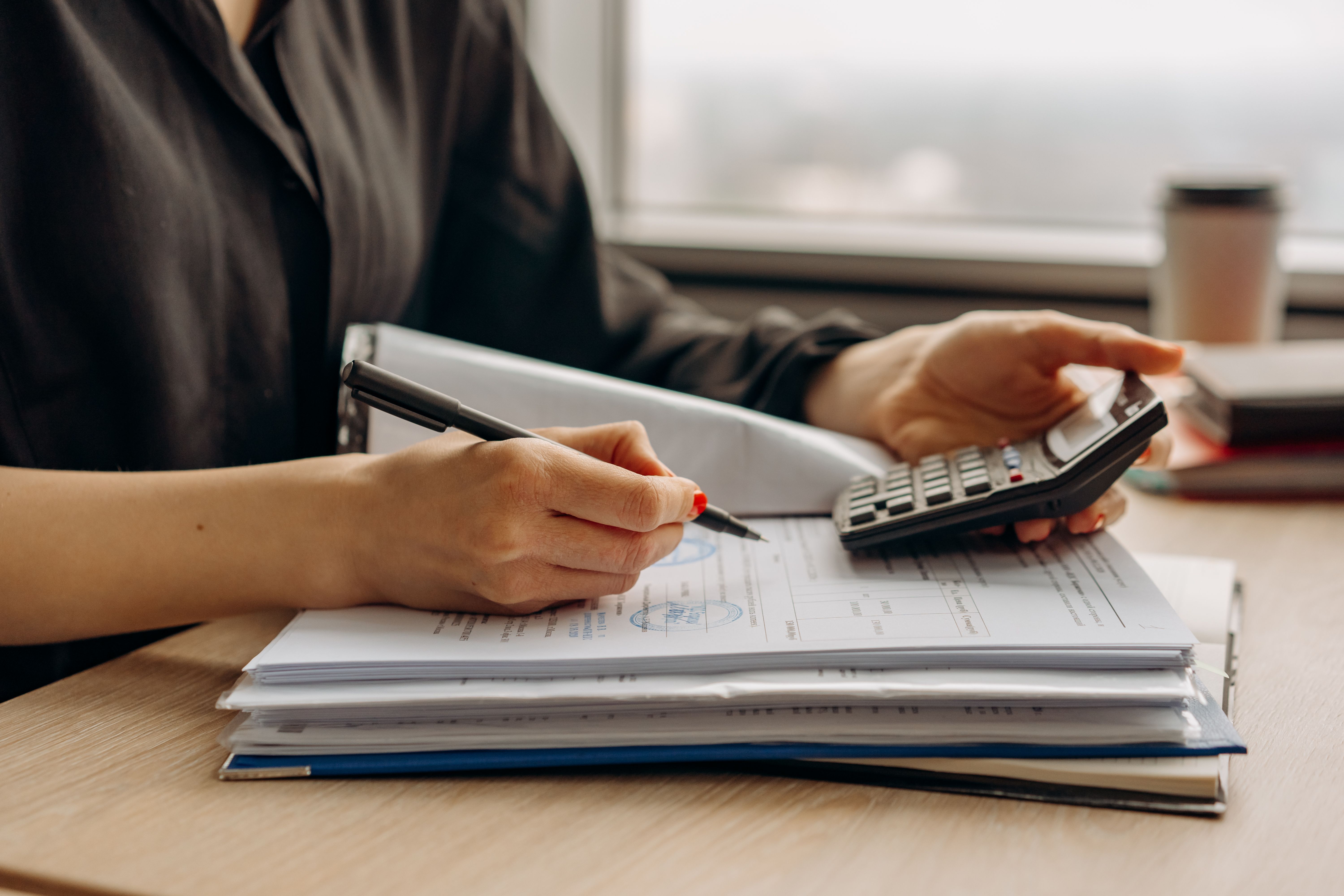 Person using a calculator alongside financial documents in an office, calculating the budget needed to finance litigation
