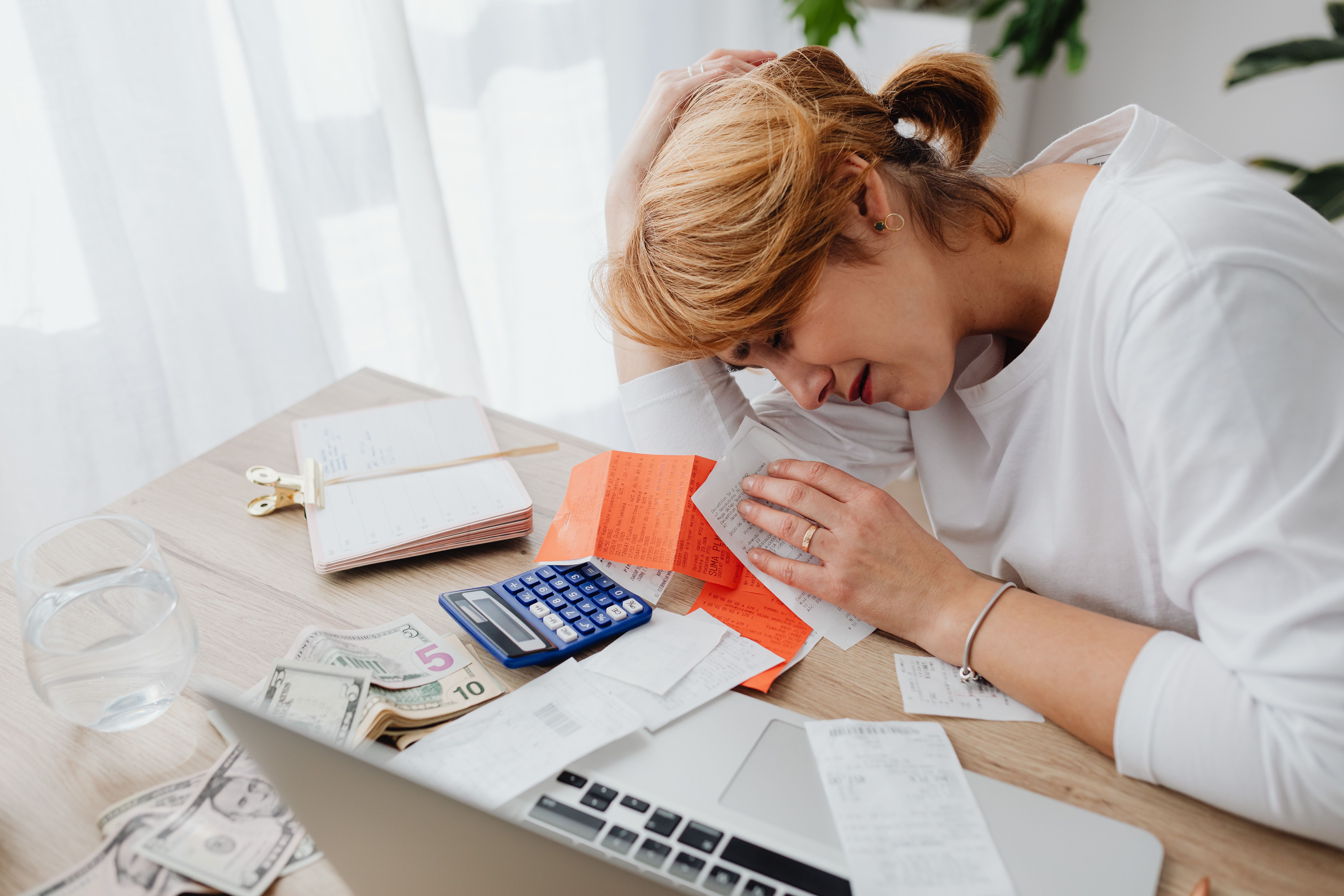 Woman overwhelmed by bills, calculator and cash at her desk, illustrating the financial strain of funding expensive litigation